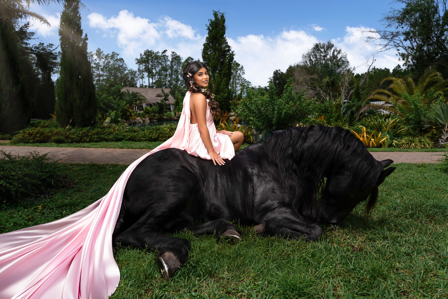 Ilyana seated on a black horse outdoors in her quinceañera gown